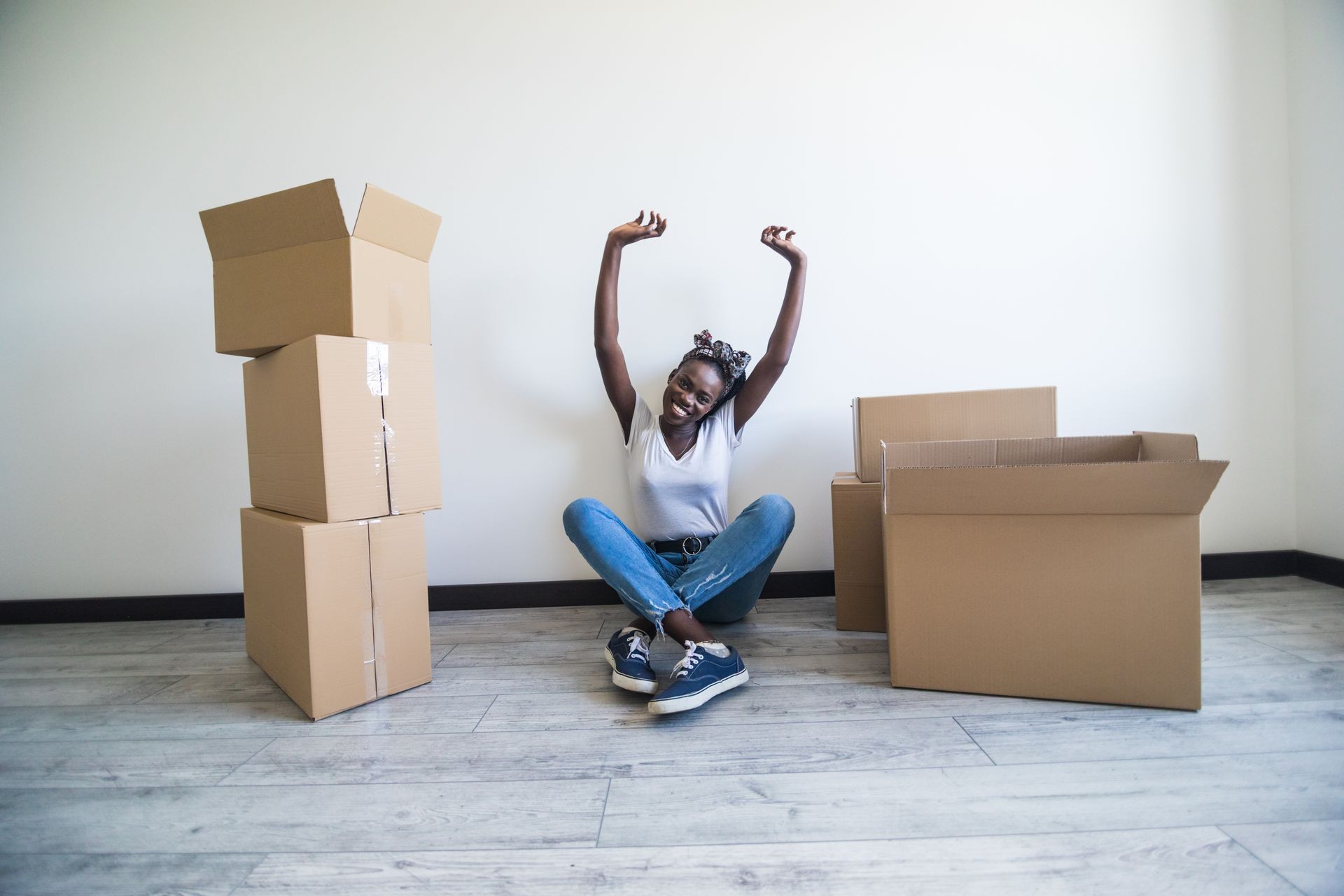 people, moving new place and repair concept - happy african american young woman with many cardboard boxes sitting on floor at home
